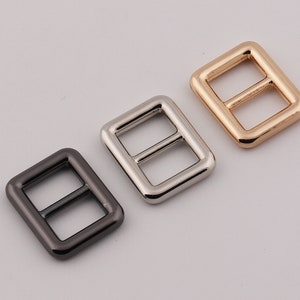 以下が含まれることがあります： 黒、銀、金の3種類の仕上げの金属製のバックル。各バックルは、丸みを帯びたエッジと中央のバーを持つ長方形です。