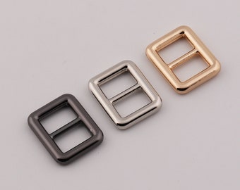 May include: Three metal buckles in different finishes: black, silver, and gold. Each buckle is rectangular with a rounded edge and a center bar.