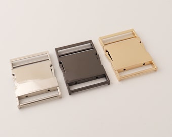 May include: Three metal belt buckles in different finishes: silver, gunmetal, and gold. Each buckle has a rectangular shape with a smooth surface and two holes on each side.