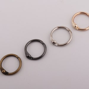 Könnte beinhalten: Vier Metall-Ordnerringe in verschiedenen Ausführungen: Antik-Messing, Schwarz, Silber und Roségold. Jeder Ring ist kreisförmig mit einer Scharnieröffnung und einem kleinen Kugelverschluss. Geeignet für Bastel- und Organisationsprojekte.