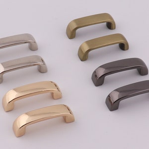May include: Assortment of metal D-ring hardware in various finishes, including silver, gold, brass, and black. The D-rings are all the same size and shape, and they are arranged in two rows of five.