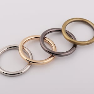 May include: Four metal rings in different finishes: silver, gold, black, and brass. The rings are interlocked, creating a decorative and functional design.