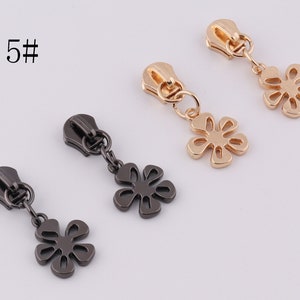 May include: Three zipper pulls with flower charms. The zipper pulls are in gold, black, and silver. The flower charms are all the same design, but in different colors.