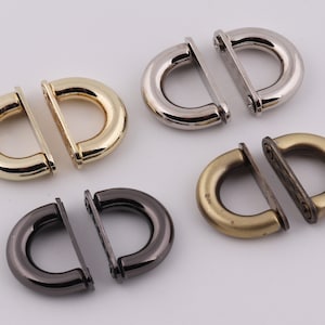 May include: Four pairs of metal D-ring clasps in different finishes: gold, silver, antique brass, and black. Each clasp is made of two pieces that connect together.