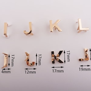 May include: Gold-colored metal letter charms in the shapes of I, J, K, and L. The charms are approximately 1.7 cm tall and 1.7 cm wide. The charms are shown on a white background.