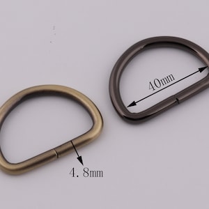 Pu&ograve; includere: Due anelli di metallo a forma di D, uno in ottone anticato e uno in nichel nero. L'anello in ottone ha un diametro di 4,8 cm e l'anello in nichel nero ha un diametro di 4 cm.