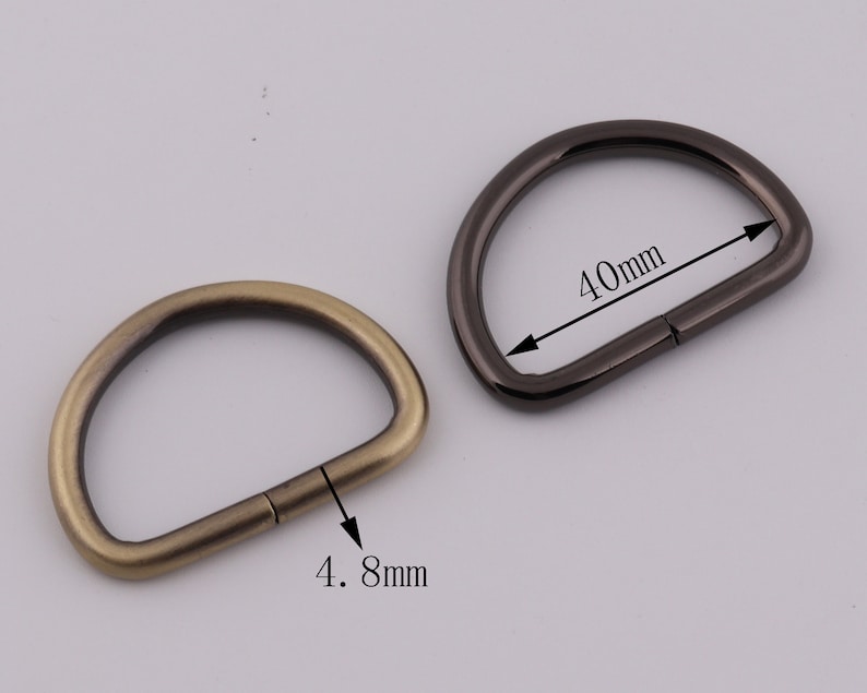 Pu&ograve; includere: Due anelli di metallo a forma di D, uno in ottone anticato e uno in nichel nero. L'anello in ottone ha un diametro di 4,8 cm e l'anello in nichel nero ha un diametro di 4 cm.