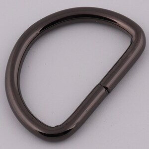 Pu&ograve; includere: Un anello a D in metallo nero con una finitura liscia. L'anello &egrave; aperto da un lato e ha un anello chiuso dall'altro.