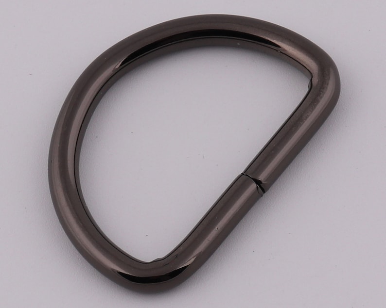 Pu&ograve; includere: Un anello a D in metallo nero con una finitura liscia. L'anello &egrave; aperto da un lato e ha un anello chiuso dall'altro.
