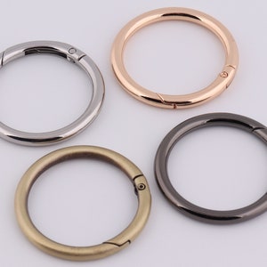 Op de afbeelding: Vier metalen sleutelringen in verschillende afwerkingen: zilver, goud, zwart en antiek messing. Elke ring heeft een draaibare sluiting.