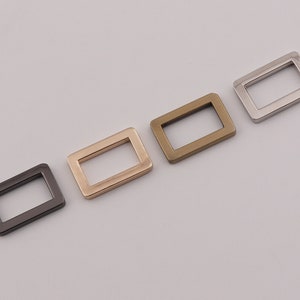 Könnte beinhalten: Vier rechteckige Metallringe in verschiedenen Ausführungen: Silber, Gold, Roségold und Schwarz.