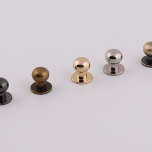 May include: Five metal knobs in different finishes: gold, brass, silver, black, and antique brass. Each knob has a round top and a flat base.