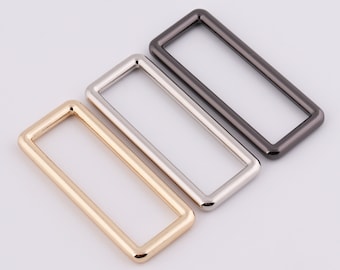 Puede incluir: Tres anillos rectangulares de metal en oro, plata y negro.