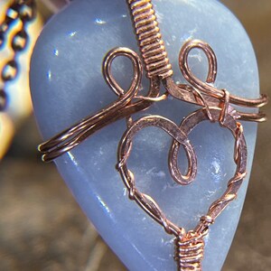 May include: A light blue heart-shaped stone pendant wrapped in copper wire with a delicate, intricate design. The pendant is attached to a copper chain.