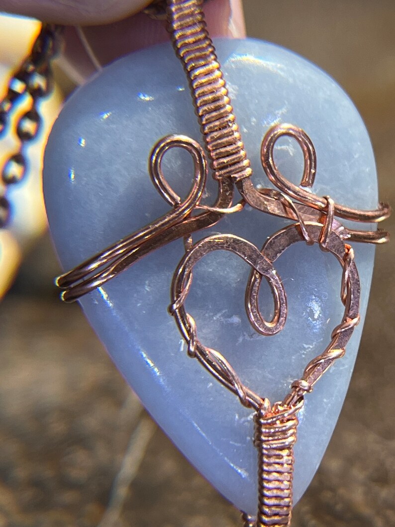May include: A light blue heart-shaped stone pendant wrapped in copper wire with a delicate, intricate design. The pendant is attached to a copper chain.