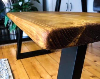 May include: A wooden table with a natural finish and black metal legs. The table has a rustic look and is made of reclaimed wood.