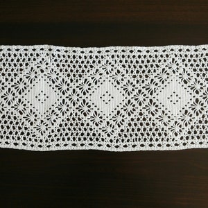 May include: White crocheted lace trim with a delicate floral pattern. The lace is approximately 2.5 cm wide and has a scalloped edge.
