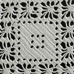 May include: White crocheted doily with a delicate floral pattern. The doily is square shaped with a central diamond design.