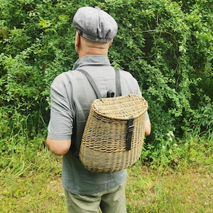 May include: A person wearing a gray newsboy cap is carrying a woven wicker backpack with black leather straps. The backpack is worn over the person's shoulders.