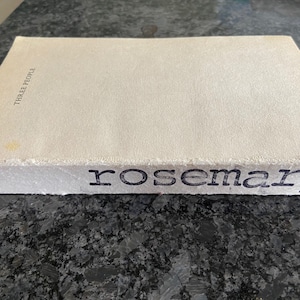 May include: A white book with the title "Three People" and the author's name "rosemary" printed on the spine.