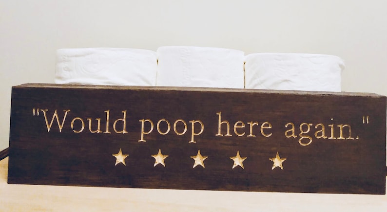 Peut inclure: Une bo&icirc;te en bois brun fonc&eacute; avec le texte "Would poop here again." et cinq &eacute;toiles dor&eacute;es. La bo&icirc;te contient trois rouleaux de papier toilette blanc.