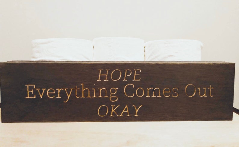 Peut inclure: Une bo&icirc;te en bois brun fonc&eacute; avec le texte "HOPE Everything Comes Out OKAY" grav&eacute; en lettres dor&eacute;es. La bo&icirc;te contient trois rouleaux de papier toilette blancs.