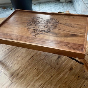 May include: A wooden folding tray with a heart-shaped design engraved with a handwritten message. The tray is made of light brown wood and has a dark brown finish. The message is in cursive and reads "I love you more than words can say".
