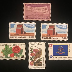 Pu&ograve; includere: Una collezione di francobolli vintage con immagini del Dakota del Nord, tra cui un elevatore di cereali, una mappa dello stato, un'allodola dei prati, una rosa selvatica di prateria e la bandiera dello stato. I francobolli sono degli anni '70 e '80.