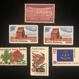 Pu&ograve; includere: Una collezione di francobolli vintage con immagini del Dakota del Nord, tra cui un elevatore di cereali, un giardino della pace, un'allodola dei prati e il sigillo dello stato. I francobolli sono del 50&deg; anniversario della stato, dell'era bicentenaria e degli anni '80.