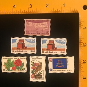 Pu&ograve; includere: Cinque francobolli vintage con immagini del Dakota del Nord. I francobolli raffigurano una mappa del Dakota del Nord, un silo per cereali, una rosa, un'allodola dei prati e il sigillo dello stato. I francobolli sono degli anni '70 e '80.