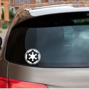 May include: A white vinyl sticker of the Galactic Empire logo on the back window of a silver car.