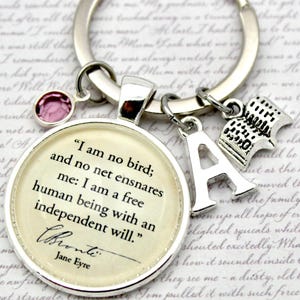 May include: Silver keyring with a quote from Jane Eyre on a round charm: "I am no bird; and no net ensnares me: I am a free human being with an independent will." Includes a pink gem and book charm.