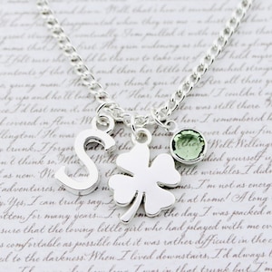 May include: A silver necklace with a charm of a four-leaf clover, a green gemstone, and a silver charm with the letter 'S'.