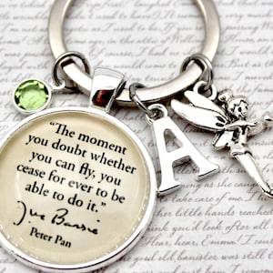 May include: Silver keyring with a round charm quoting Peter Pan, a green gem, a letter "A" charm, and a Tinkerbell charm. The quote reads: "The moment you doubt whether you can fly, you cease for ever to be able to do it."