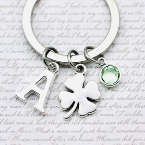 May include: Silver keyring with a letter A charm, a four-leaf clover charm, and a light green crystal charm.