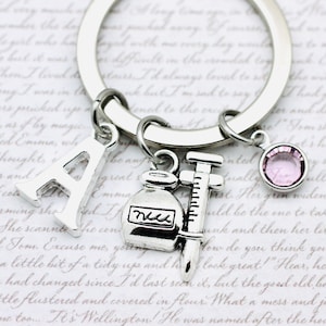 May include: A silver keyring with a charm of the letter A, a charm of a bottle with the word "med" on it, a charm of a syringe, and a pink rhinestone charm.
