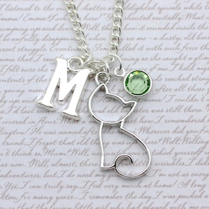 May include: A silver charm necklace with a letter 'M' charm, a silver cat charm, and a light green crystal charm. The necklace is on a white background with text.