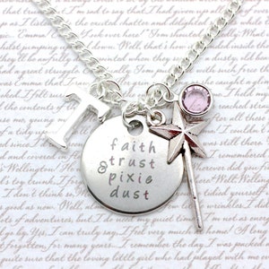 May include: Silver necklace with a charm that reads "faith & trust pixie dust". The charm is a round disc with a silver star and a pink crystal charm attached to the chain.
