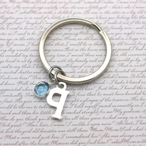 May include: A silver keychain with a light blue crystal charm and a silver letter 'P' charm. The keychain is on a white background with a handwritten note.