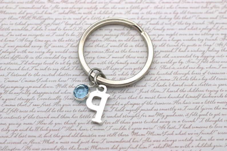 May include: A silver keychain with a light blue crystal charm and a silver letter 'P' charm. The keychain is on a white background with a handwritten note.