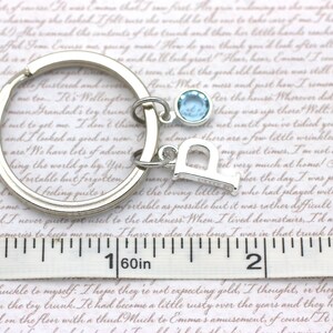 May include: A silver key chain with a light blue charm and a silver letter 'D' charm. The keychain is measured on a ruler, showing it is 1 1/16 inches long.