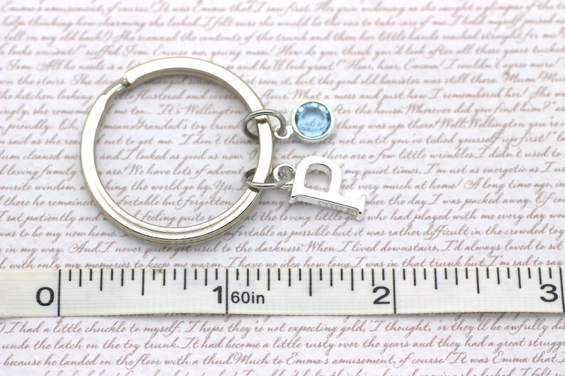May include: A silver key chain with a light blue charm and a silver letter 'D' charm. The keychain is measured on a ruler, showing it is 1 1/16 inches long.