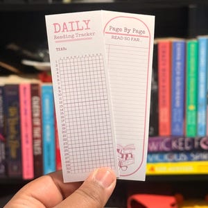 Peut inclure: Deux marque-pages blancs sont tenus devant une étagère. Le marque-page de gauche est intitulé "DAILY Reading Tracker" et celui de droite "Page By Page READ SO FAR...". L'arrière-plan comprend des livres colorés.