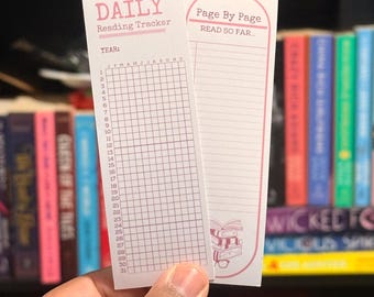 Może przedstawiać: Dwa białe trackery do czytania są trzymane przed półką z książkami. Tracker po lewej stronie jest oznaczony jako "DAILY Reading Tracker", a po prawej stronie jako "Page By Page READ SO FAR...". Tło obejmuje kolorowe książki.