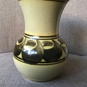 May include: A light green ceramic vase with a brown and black abstract design. The vase has a wide mouth and a rounded body.