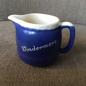 Op de afbeelding: Een blauwe keramische roomkan met een witte rand en het woord "Windermere" in wit op de zijkant.