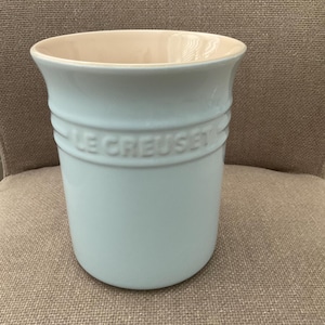 Peut inclure: Un pot à ustensiles Le Creuset bleu clair. Le pot cylindrique a une large ouverture et un intérieur crème. Le nom de la marque est en relief au milieu. En céramique.