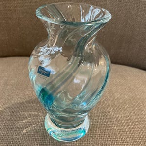 Puede incluir: Un jarrón de vidrio transparente con un diseño en espiral y una base redonda. El jarrón tiene un tinte azul claro y una etiqueta que dice "Caithness Scotland". El jarrón mide aproximadamente 15 cm de alto.