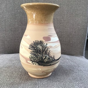 Könnte beinhalten: Eine Keramikvase mit einer hellbraunen und beigefarbenen Marmorierung. Die Vase hat eine breite Öffnung und einen schmalen Boden. Auf der Seite der Vase ist eine schwarze Silhouette eines Baumes gemalt.