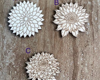 May include: Three light-coloured wooden flower cutouts labelled A, B, and C. Each piece features a detailed laser-engraved floral pattern with numerous petals. Item A is a symmetrical bloom, while B and C include additional leaf-like details.